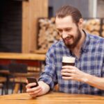 Persona revisando su teléfono en una taproom mientras sostiene una cerveza artesanal