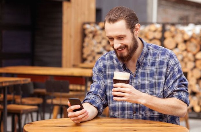 Persona revisando su teléfono en una taproom mientras sostiene una cerveza artesanal