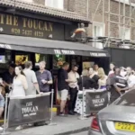 Gente bebiendo cerveza de pie junto a un pub en Soho, Londres