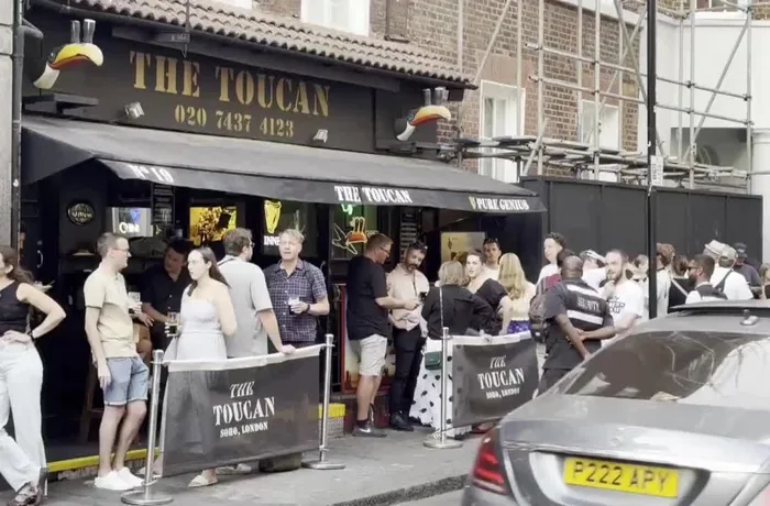 Gente bebiendo cerveza de pie junto a un pub en Soho, Londres