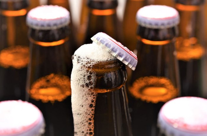 Botella de cerveza abierta rebosando espuma junto a otras botellas selladas