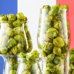Copas de cerveza llenas de conos de lúpulo francés de Alsacia, con la bandera de Francia de fondo