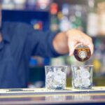 Camarero sirviendo whisky en vasos con hielo en la barra de un bar de Gran Bretaña
