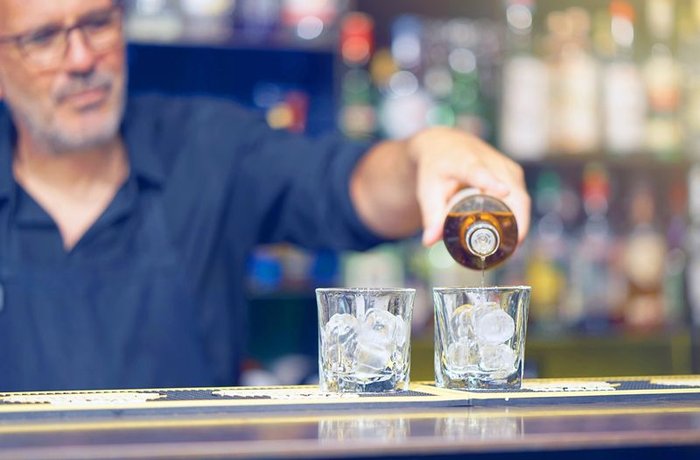Camarero sirviendo whisky en vasos con hielo en la barra de un bar de Gran Bretaña