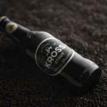 Botella de Kross Stout sobre granos de malta tostada, cerveza chilena medalla de oro