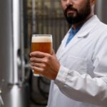 Investigador con un vaso de cerveza en una sala de fermentación, estudio del CIAD sobre biogás a partir de residuos cerveceros en México